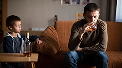 Мужчина пьет алкоголь, а ребенок рядом грустно на него смотрит